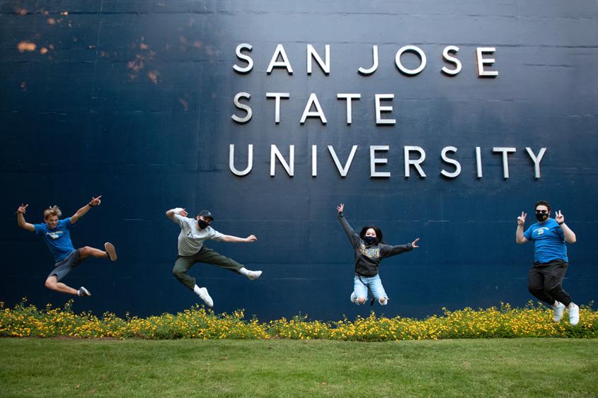 SJSU students in masks jumping mid-air in front of the WSQ building.