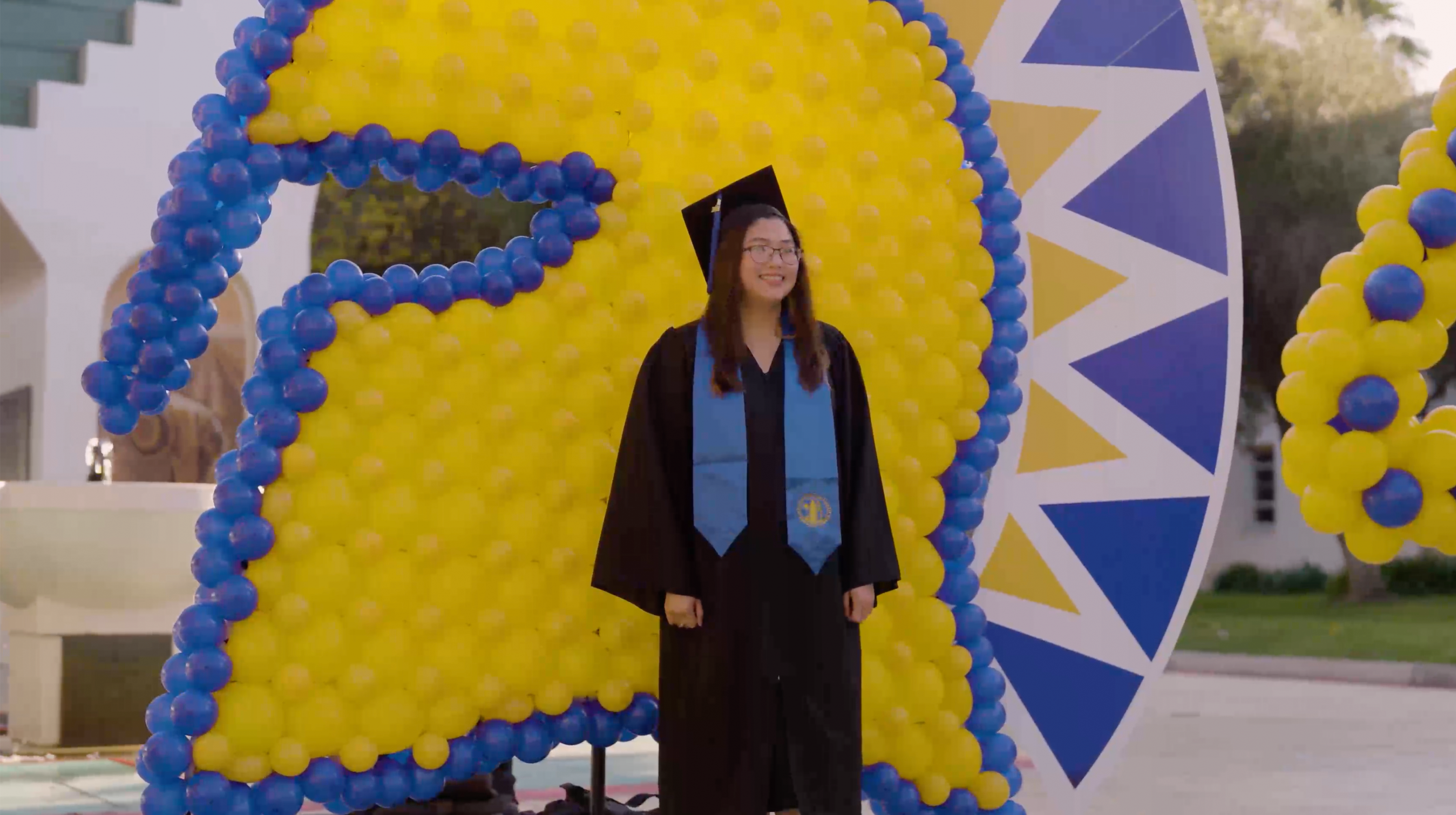 Still of a graduate gettting their photo taken at a balloon art spartan backdrop