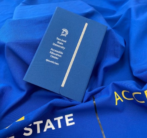 Picture of a Blue Accessible Education Notebook on top of a blue fabric