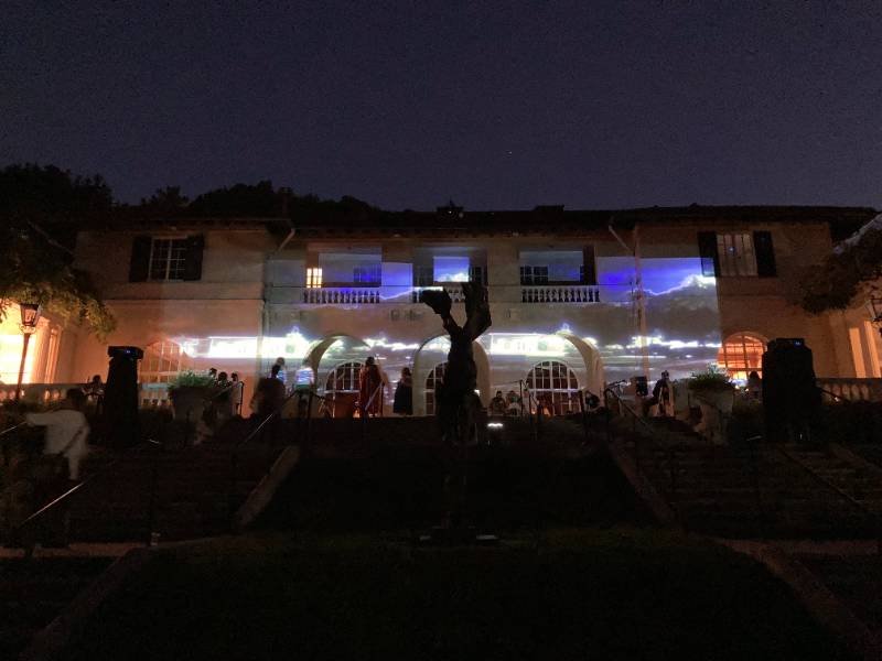 Photograph of people standing in front of a building with an image of a landscape projected onto the front facade.