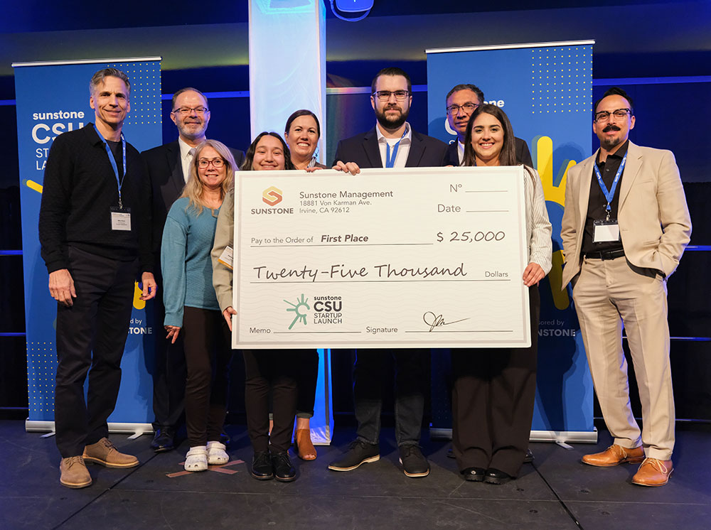 Five college-age startup founders pose onstage with two sponsors, two hosts, and a giant check for $25,000