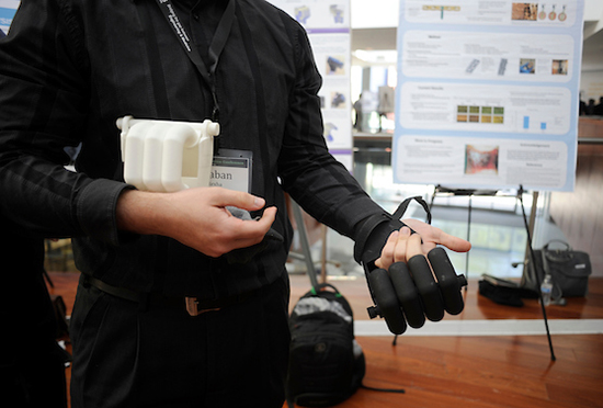 person shows off prosthetic hand with research poster in background