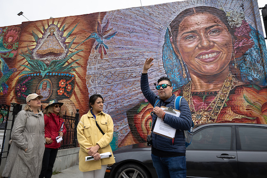 person gives tour near colorful mural with ancestor on it
