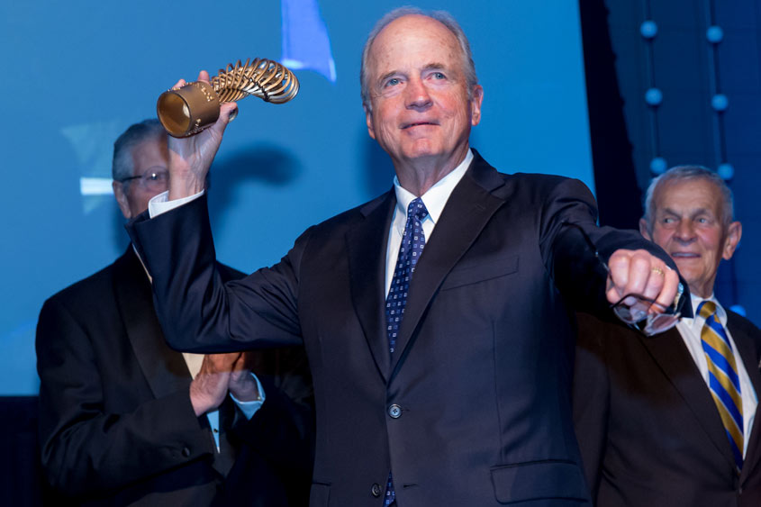 Peter Ueberroth holding an award as in pitching a ball.